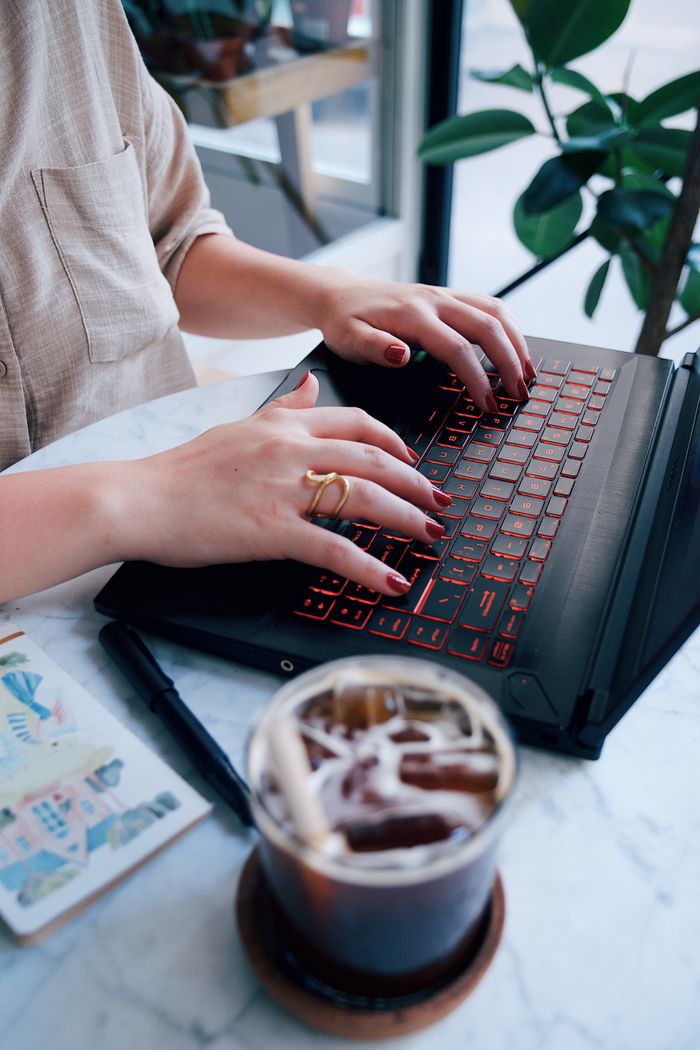 A woman typing on a laptop with a red keyboard in a café setting, enjoying iced coffee.